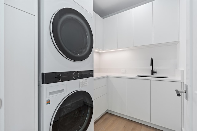 laundry room with stacked washer / drying machine, cabinets, light wood-type flooring, and sink