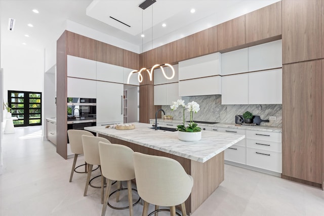 kitchen with sink, tasteful backsplash, pendant lighting, a kitchen island with sink, and white cabinets