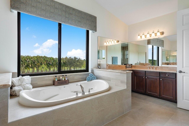 bathroom with tile patterned floors, vanity, a relaxing tiled tub, and lofted ceiling