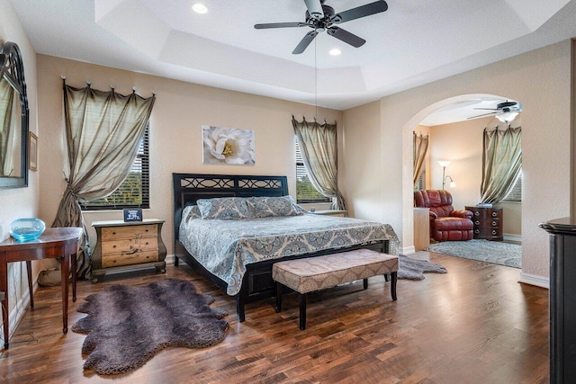 bedroom with ceiling fan, dark hardwood / wood-style floors, and a raised ceiling