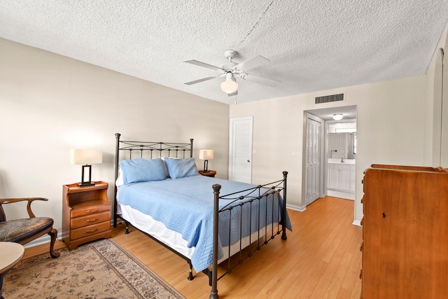 bedroom featuring wood-type flooring, a closet, ensuite bathroom, ceiling fan, and a textured ceiling