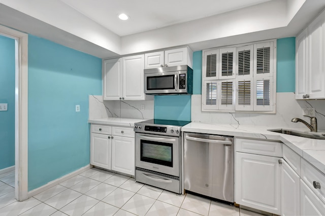 kitchen with light stone countertops, white cabinetry, stainless steel appliances, sink, and light tile floors