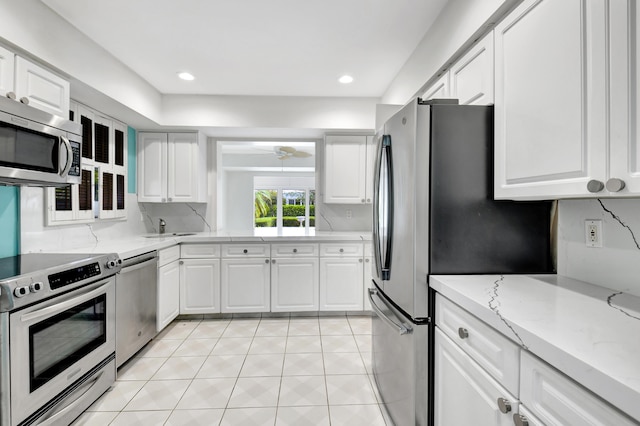 kitchen with appliances with stainless steel finishes, ceiling fan, white cabinets, light tile flooring, and light stone countertops