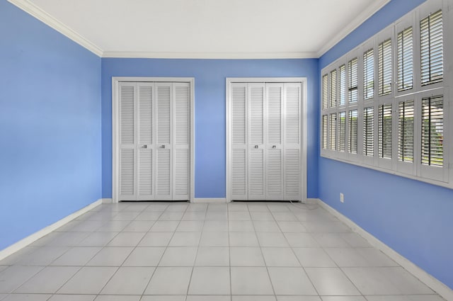 unfurnished bedroom with ornamental molding, two closets, and light tile floors