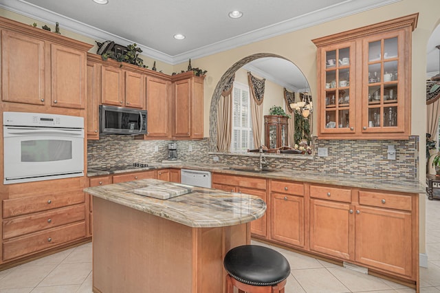 kitchen with white appliances, sink, light tile patterned floors, ornamental molding, and a kitchen island