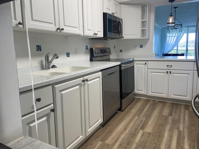 kitchen with pendant lighting, dark wood finished floors, appliances with stainless steel finishes, white cabinetry, and a sink