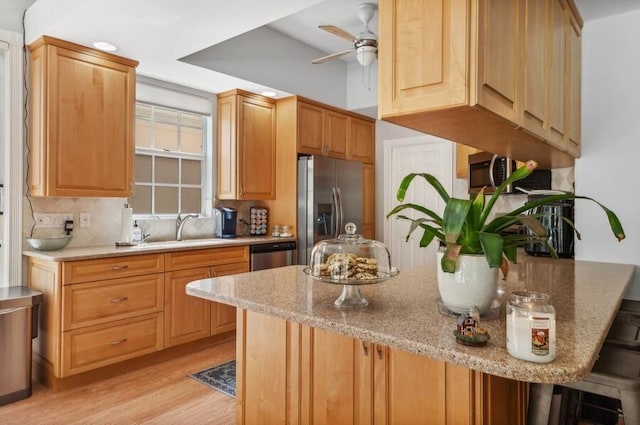 kitchen with a kitchen breakfast bar, backsplash, appliances with stainless steel finishes, light hardwood / wood-style floors, and ceiling fan