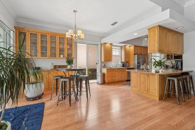 kitchen with kitchen peninsula, light hardwood / wood-style flooring, stainless steel appliances, a chandelier, and a breakfast bar