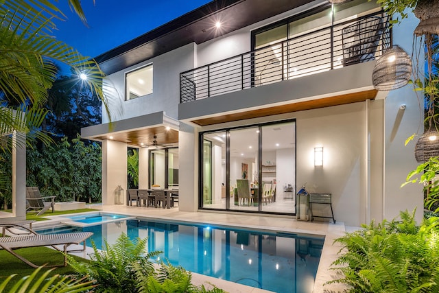 back house at twilight with a patio, ceiling fan, a balcony, and a pool with hot tub