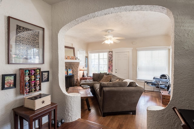 living room with ceiling fan, dark hardwood / wood-style floors, a textured ceiling, and a fireplace