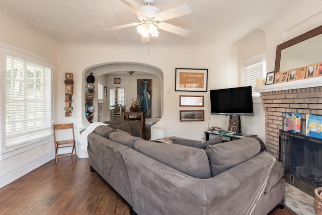 living room featuring wood-type flooring, a brick fireplace, ceiling fan, and a textured ceiling