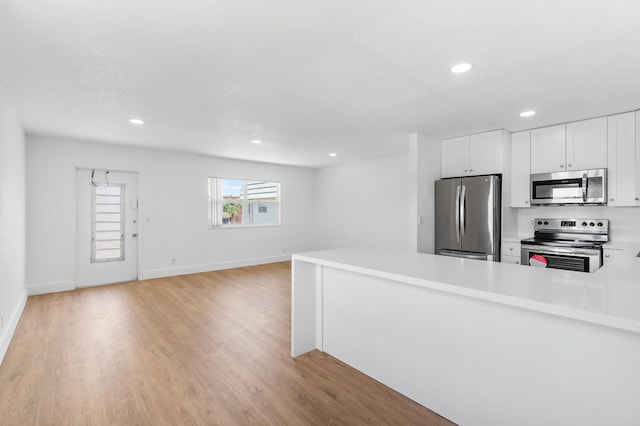 kitchen featuring kitchen peninsula, light wood-type flooring, a textured ceiling, stainless steel appliances, and white cabinets