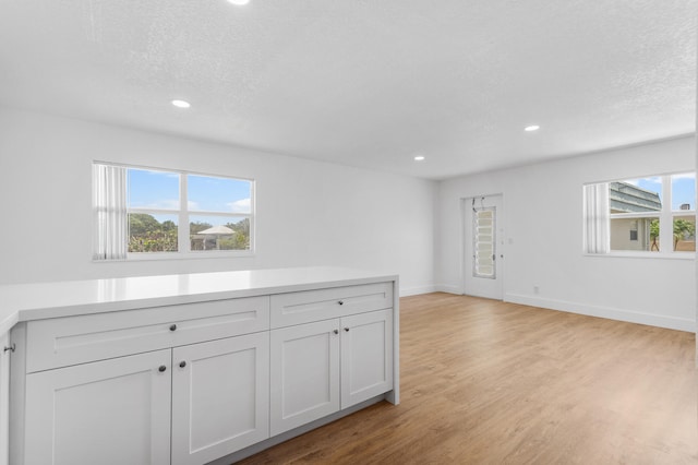 interior space featuring white cabinets, a textured ceiling, light hardwood / wood-style flooring, and a healthy amount of sunlight