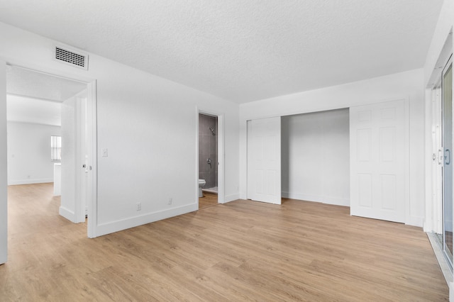 unfurnished bedroom with light wood-type flooring, a textured ceiling, connected bathroom, and a closet