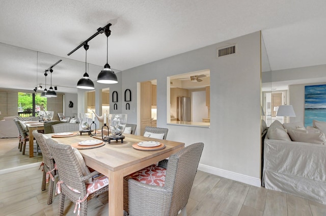 dining area featuring a textured ceiling, rail lighting, and light hardwood / wood-style flooring