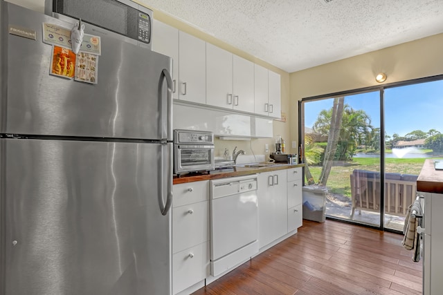 kitchen featuring white cabinets, stainless steel appliances, a textured ceiling, hardwood / wood-style floors, and sink