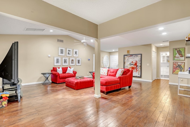 living room featuring light wood-type flooring, lofted ceiling, ceiling fan, and a textured ceiling