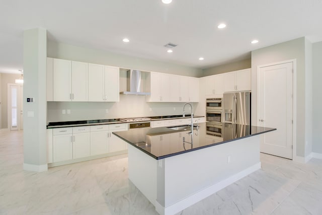 kitchen featuring wall chimney range hood, stainless steel appliances, white cabinetry, an island with sink, and sink