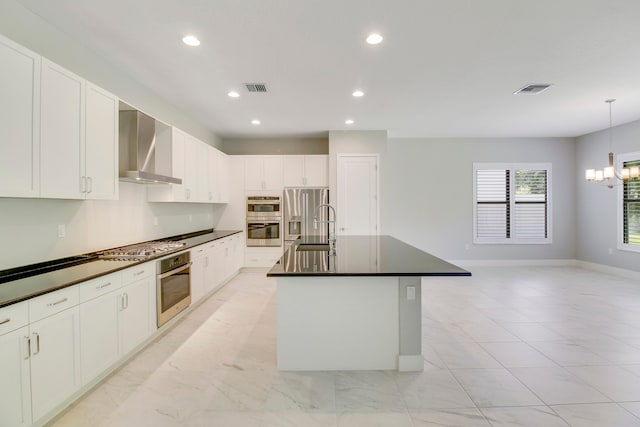 kitchen with a center island with sink, white cabinetry, wall chimney exhaust hood, appliances with stainless steel finishes, and light tile floors