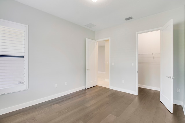 unfurnished bedroom featuring a closet, a spacious closet, and dark hardwood / wood-style floors