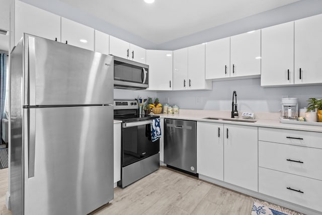 kitchen with sink, white cabinets, appliances with stainless steel finishes, and light wood-type flooring