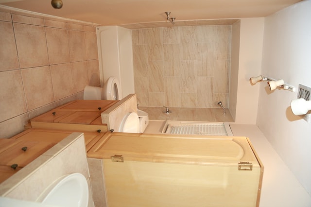 bathroom with tiled shower / bath, toilet, and tile walls