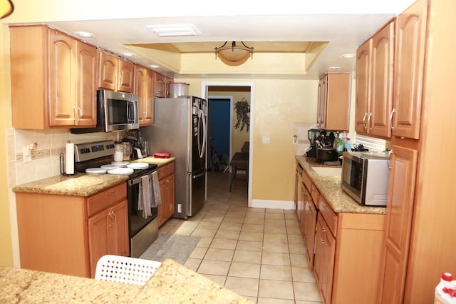 kitchen featuring stainless steel appliances, light stone counters, backsplash, light tile flooring, and a raised ceiling