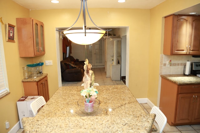 kitchen with light stone counters, hanging light fixtures, tasteful backsplash, and light tile floors