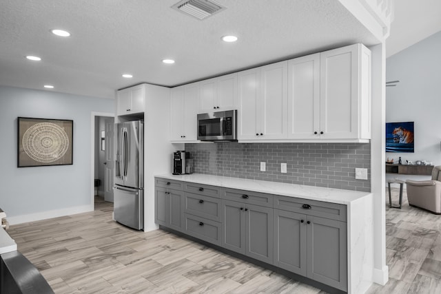 kitchen featuring white cabinetry, light hardwood / wood-style floors, stainless steel appliances, gray cabinets, and light stone counters