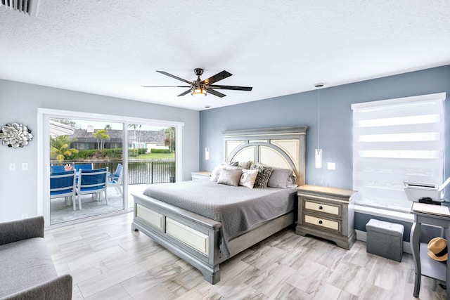 bedroom featuring a water view, ceiling fan, access to outside, and a textured ceiling