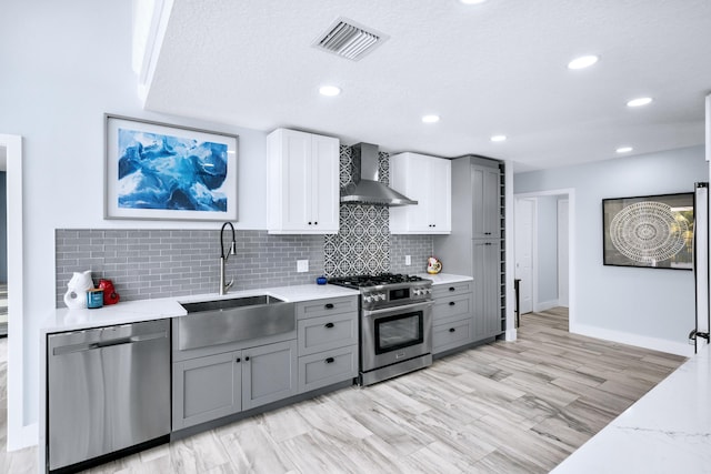 kitchen featuring stainless steel appliances, wall chimney range hood, sink, and gray cabinets