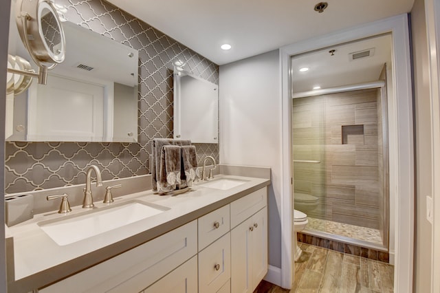 bathroom featuring wood-type flooring, a shower with door, double sink vanity, tasteful backsplash, and toilet