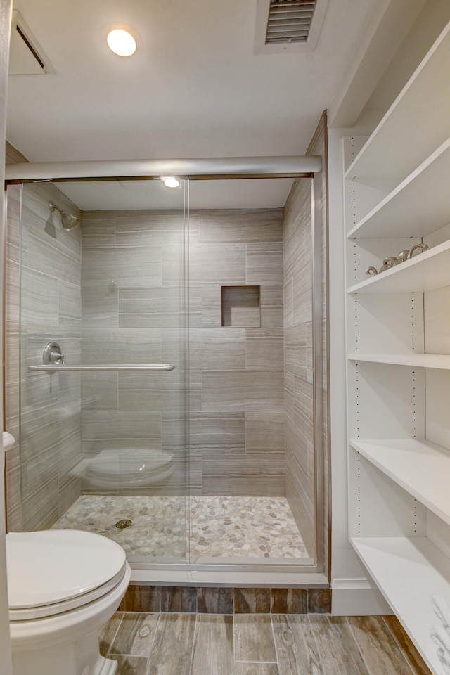 bathroom with hardwood / wood-style flooring, a shower with door, and toilet