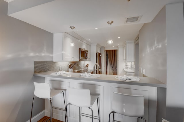 kitchen featuring kitchen peninsula, decorative light fixtures, backsplash, stainless steel appliances, and white cabinets