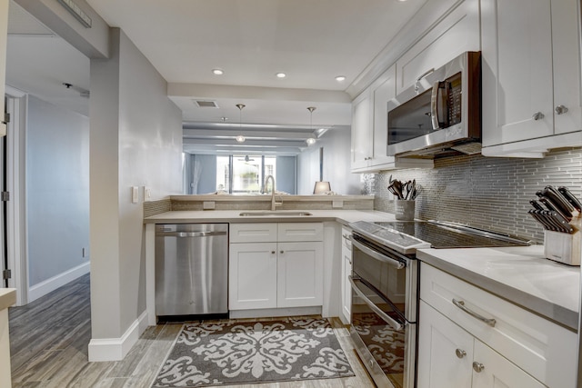 kitchen with backsplash, stainless steel appliances, white cabinetry, sink, and light wood-type flooring