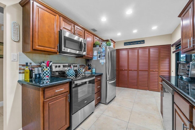 kitchen featuring backsplash, appliances with stainless steel finishes, dark stone countertops, and light tile flooring