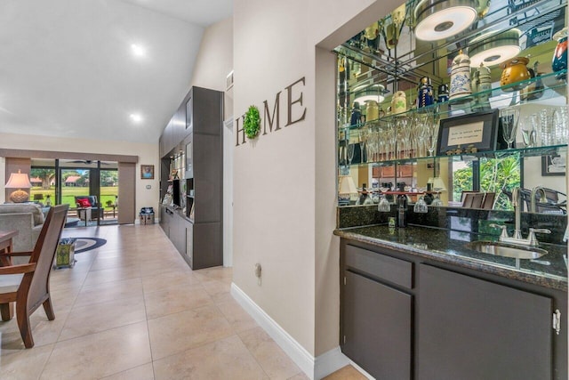 bar featuring high vaulted ceiling, sink, dark stone counters, and light tile flooring