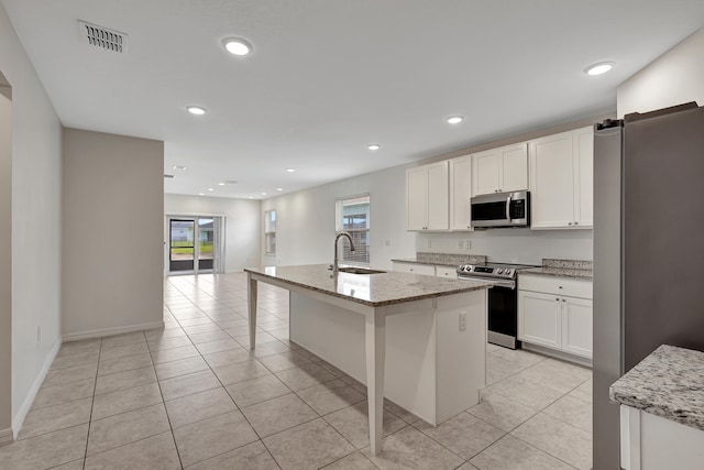 kitchen with a healthy amount of sunlight, a center island with sink, appliances with stainless steel finishes, and light stone countertops