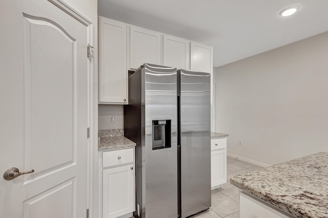 kitchen with light stone counters, stainless steel refrigerator with ice dispenser, white cabinetry, and light tile floors