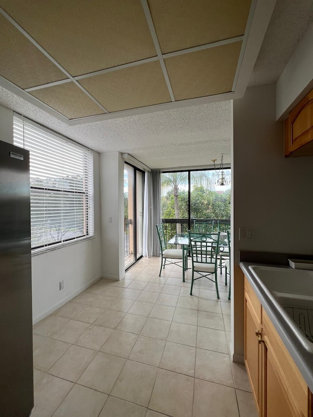 kitchen with a textured ceiling, stainless steel refrigerator, light tile floors, and expansive windows