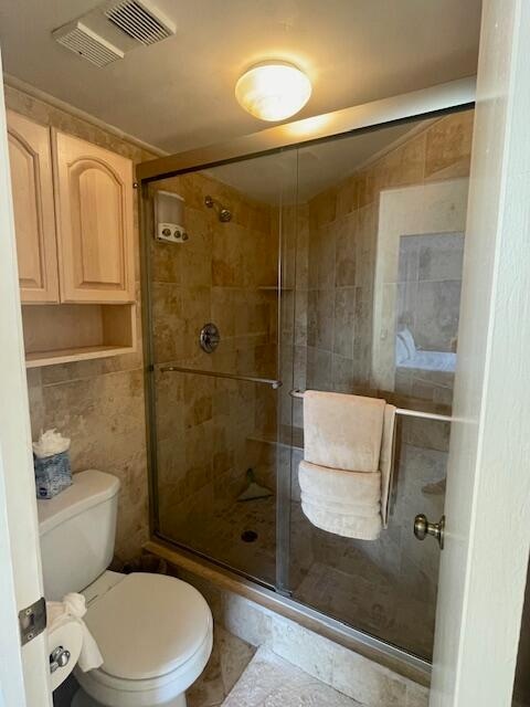 bathroom featuring tile floors, walk in shower, toilet, and tile walls