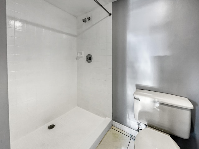 bathroom with tile flooring, tiled shower, and toilet