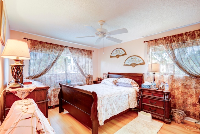 bedroom with a textured ceiling, multiple windows, light wood-type flooring, and ceiling fan