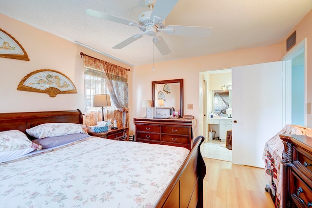 bedroom featuring a textured ceiling, ensuite bathroom, light wood-type flooring, and ceiling fan