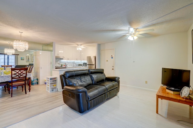 living room featuring light hardwood / wood-style floors, a textured ceiling, and ceiling fan with notable chandelier