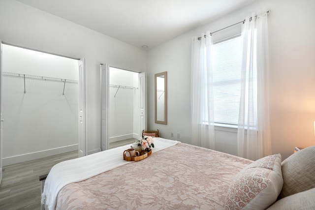 bedroom with wood finished floors, multiple closets, and baseboards