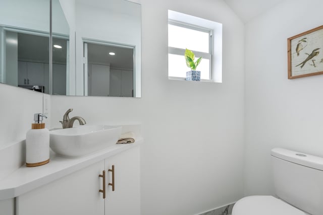 bathroom featuring toilet, vanity, and vaulted ceiling