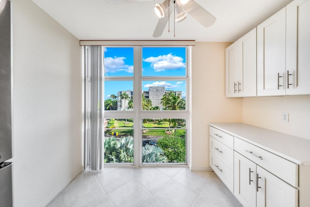 interior space with white cabinets, ceiling fan, light tile patterned floors, and expansive windows