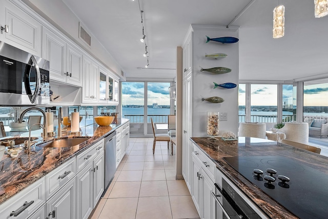 kitchen with white cabinetry, appliances with stainless steel finishes, dark stone counters, track lighting, and light tile floors