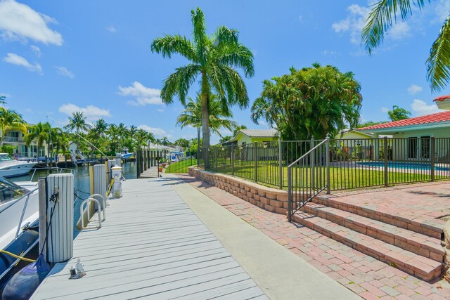 view of property's community with a lawn, a pool, a water view, a dock, and a patio